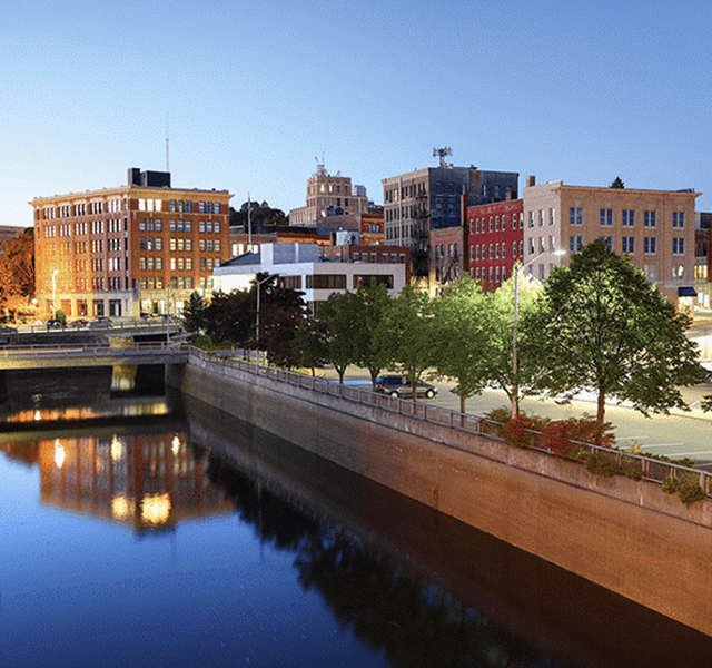 group of small brick buildings with a water canal in the front. There are trees along the canal and lights reflecting off the water.